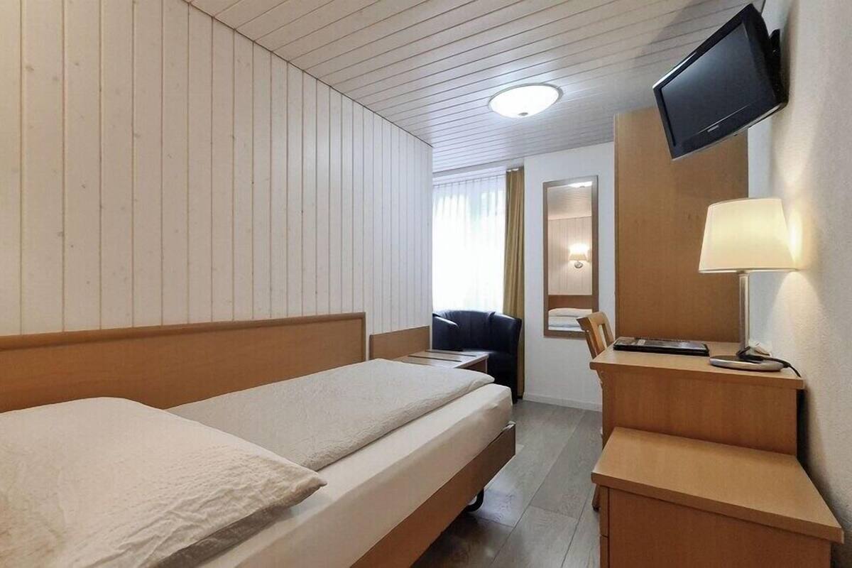 Una habitación de hotel con una cama litera de madera, un escritorio con lámpara, un televisor montado en la pared y un espejo.