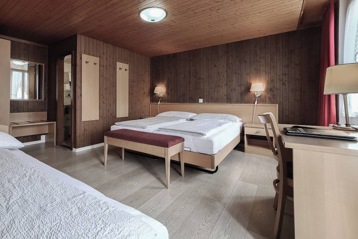 Habitación de hotel con dos camas, un escritorio, una silla, un banco y un armario.
