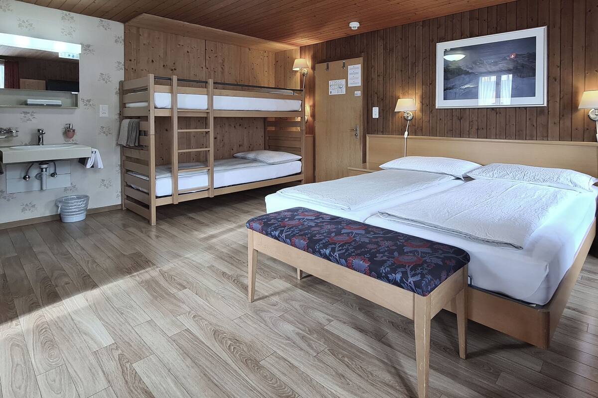 Una habitación tipo cabaña de madera con literas, una cama grande, un banco, un lavabo y un espejo.