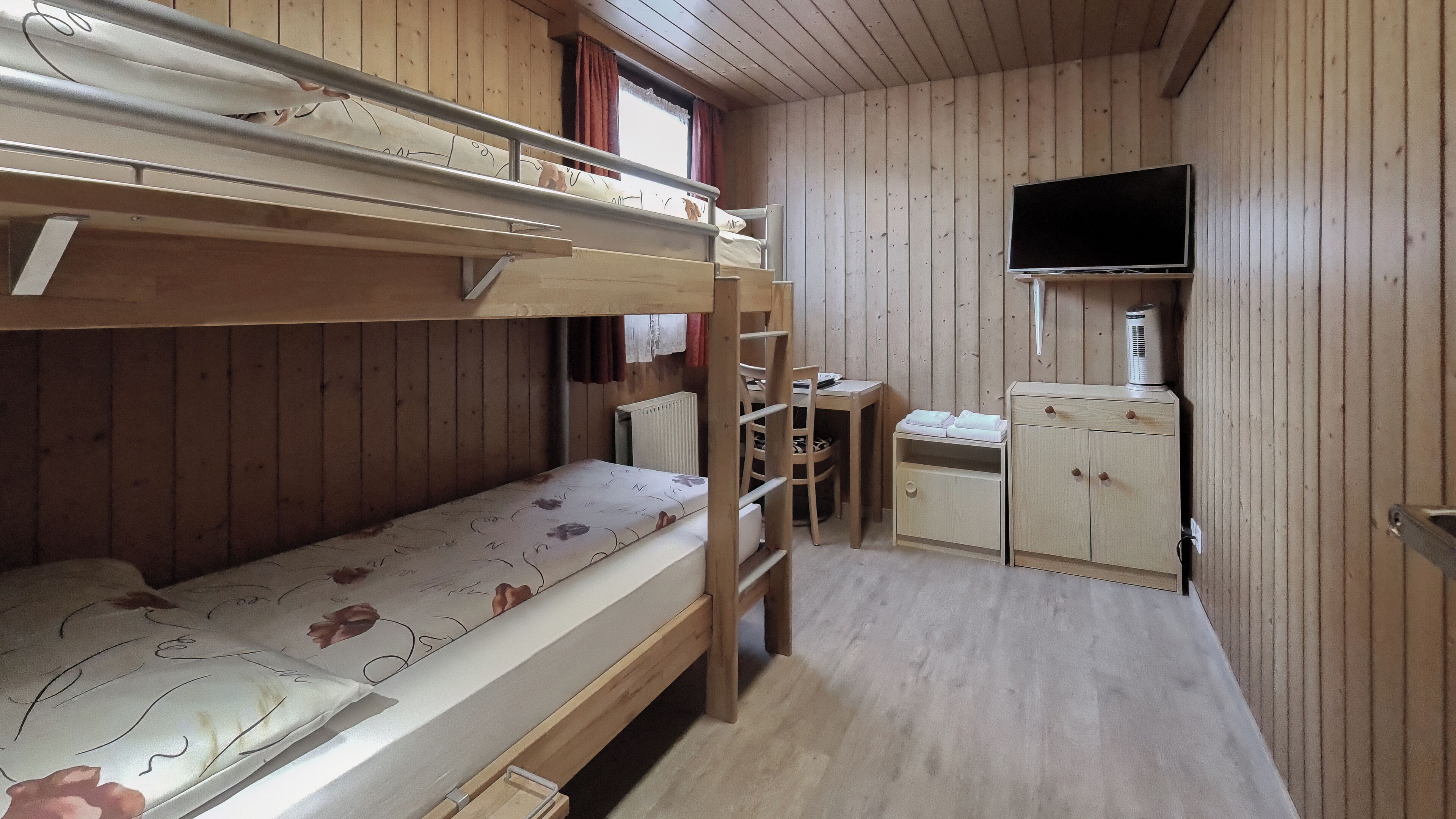 A bunk bed room with a desk and a TV.