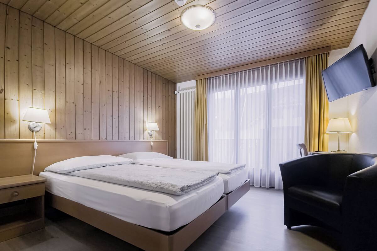 Habitación de hotel con techo de madera, dos camas, un televisor y un escritorio con lámpara.