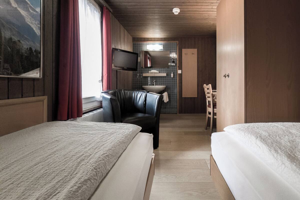 Habitación de hotel con dos camas, un sofá, televisión y baño visible a través de una puerta abierta.