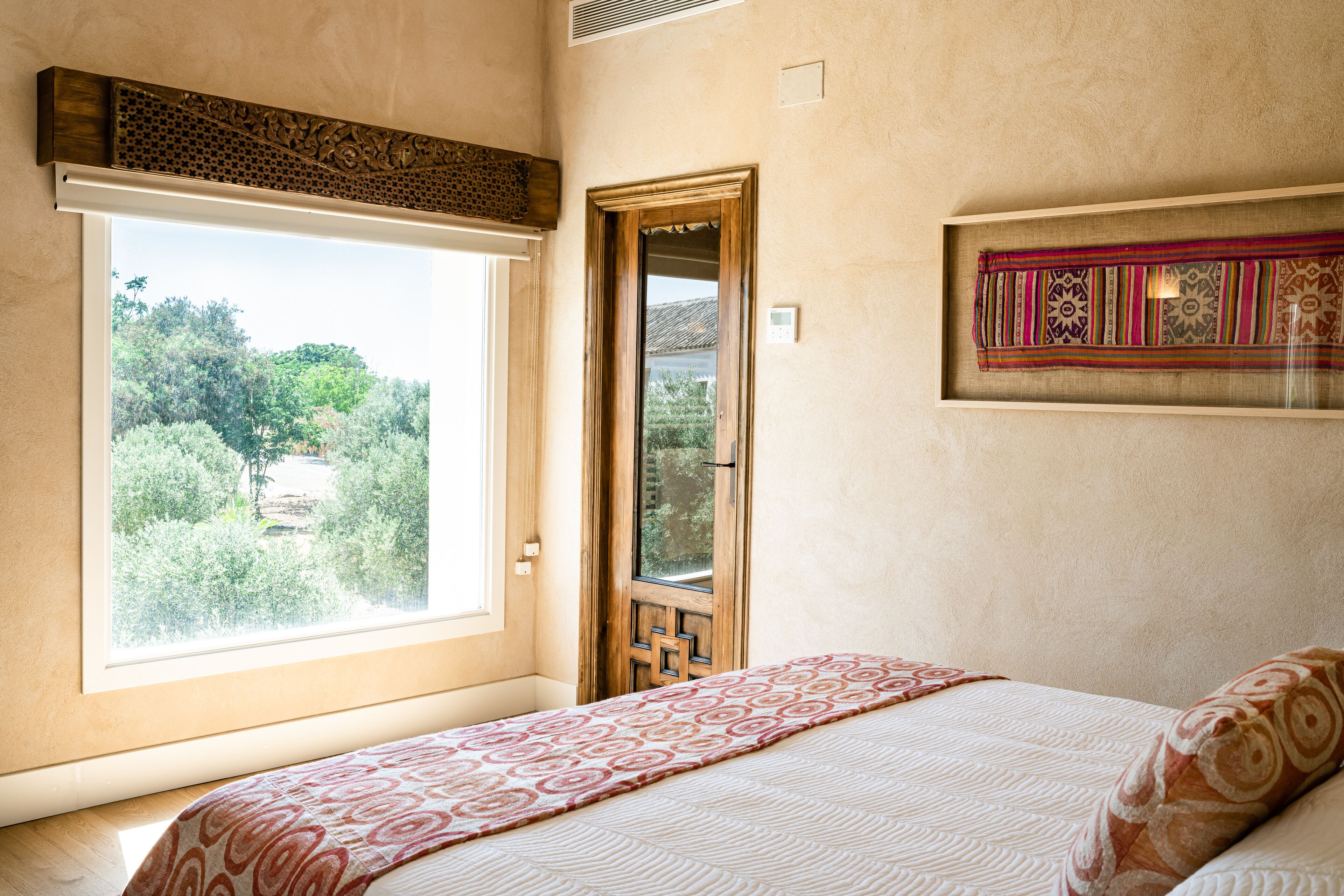 Un dormitorio con un ventanal grande, una cama con ropa de cama estampada y un adorno en la pared.
