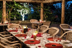 A dining table set with red placemats, glassware, and wicker chairs in an outdoor setting.