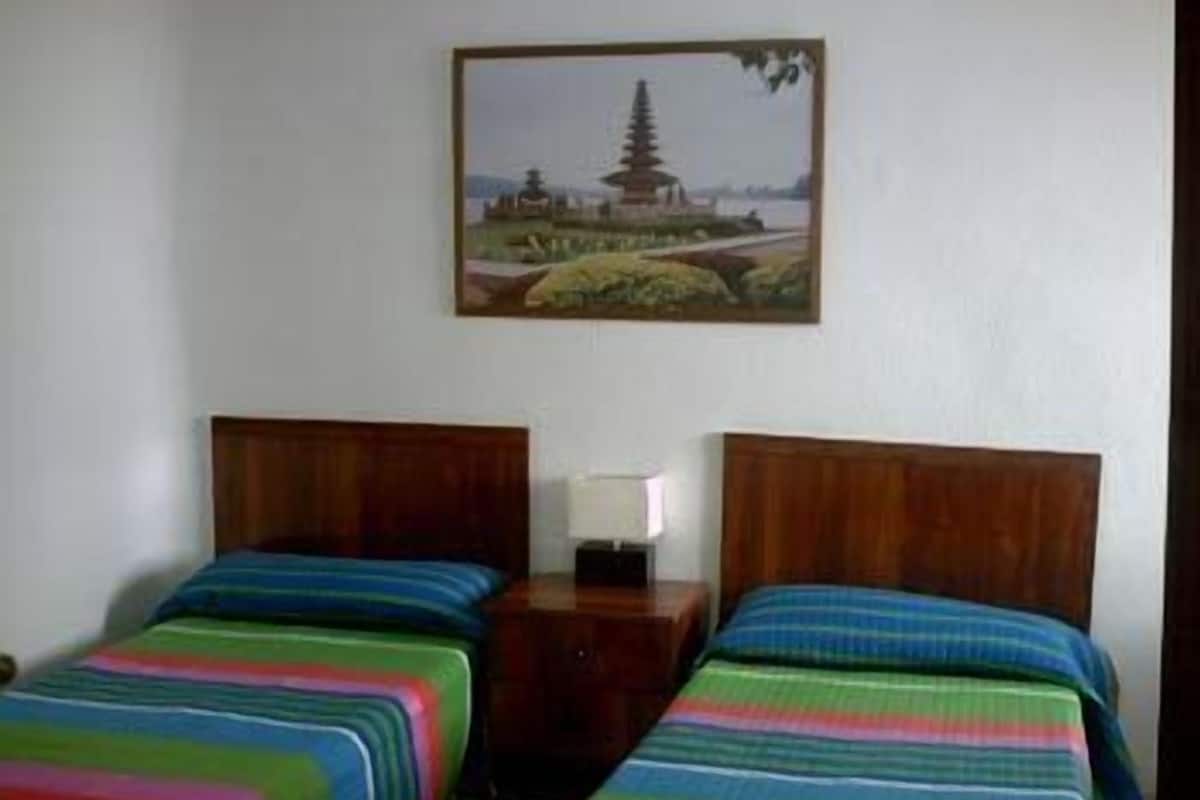 A room with two beds, each with colorful striped bedding. There is a painting of a pagoda on the wall.