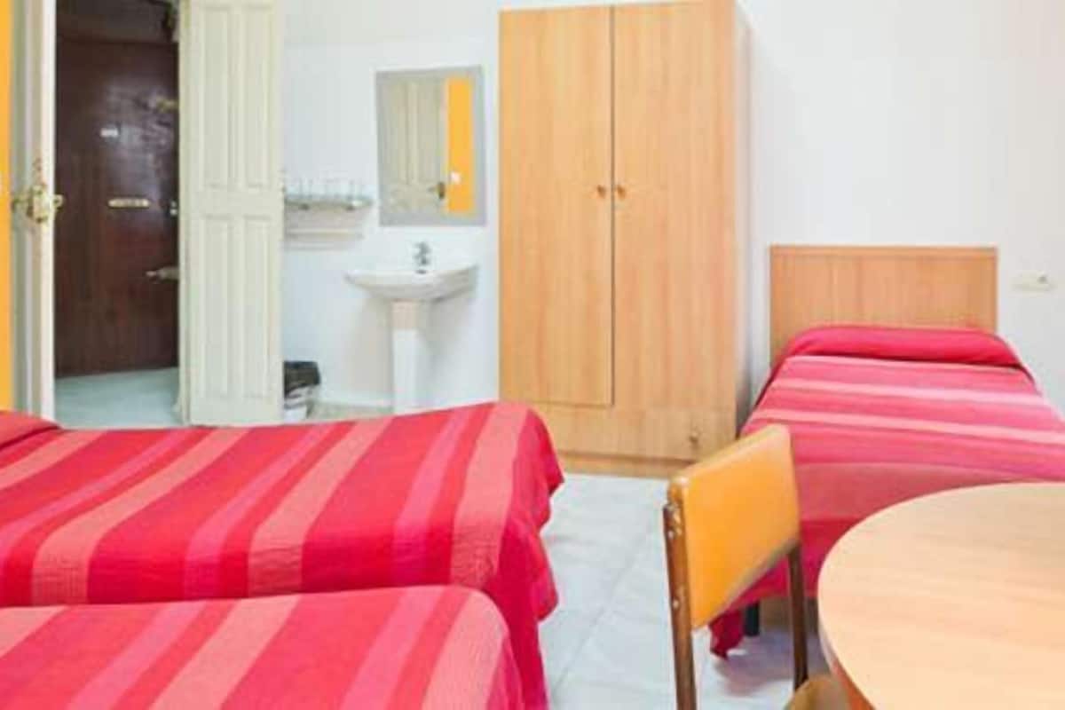 A hotel room with two beds, a wooden wardrobe, a round table, and a single chair.