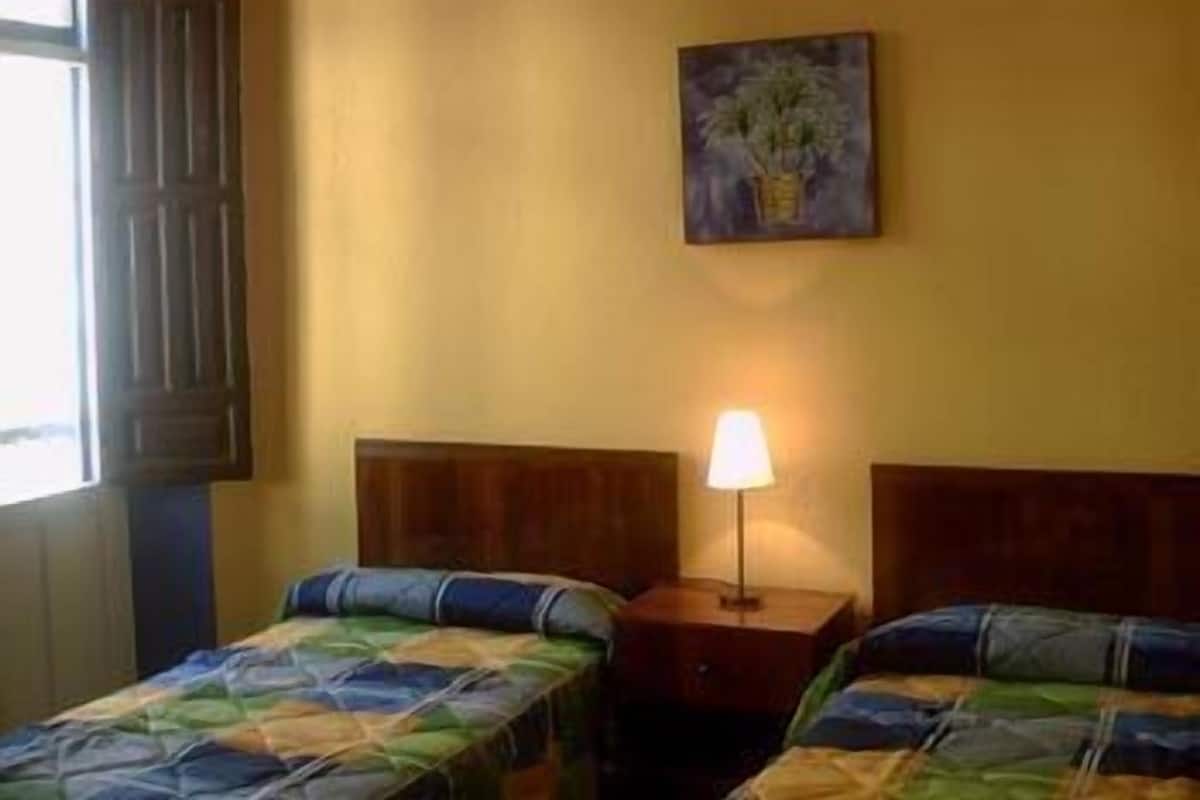 A room with two beds, a nightstand with a lamp, and a painting on the wall.