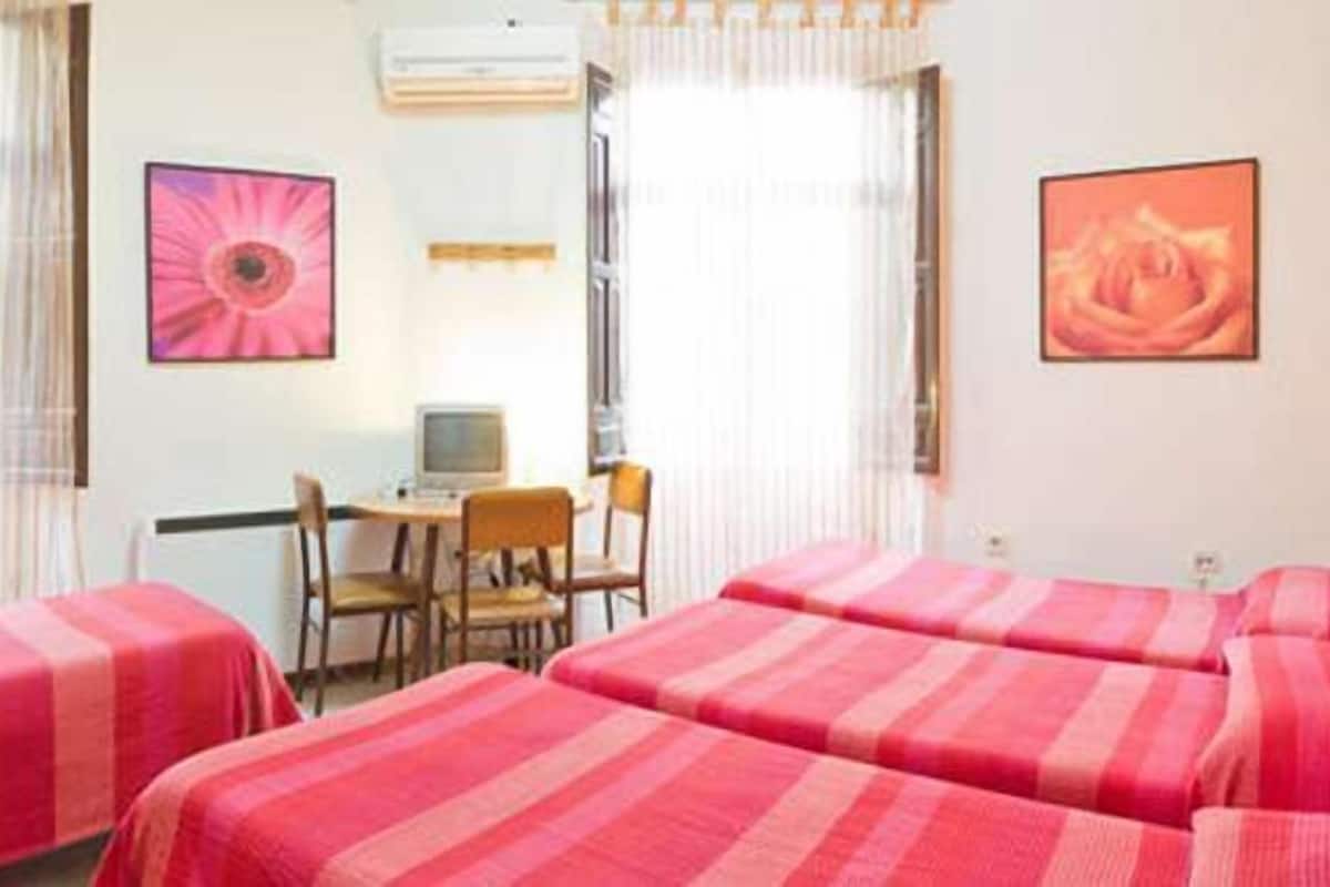 A hotel room with two single beds, a desk with a chair, a computer, and two framed pictures on the wall.