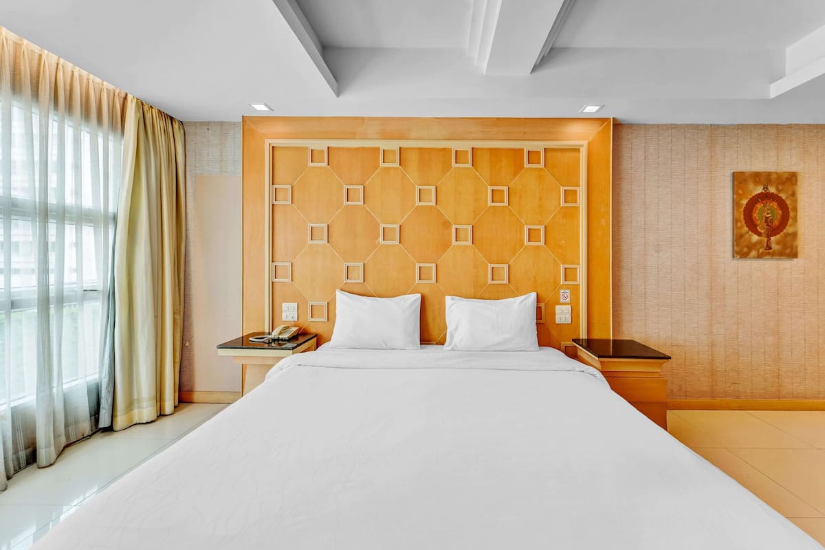 A hotel room with a large bed, a wooden headboard, a nightstand, and a window with curtains.