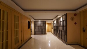 Un couloir d’hôtel avec un sol carrelé, des lambris en bois sur les murs et une porte portant une plaque avec un numéro.