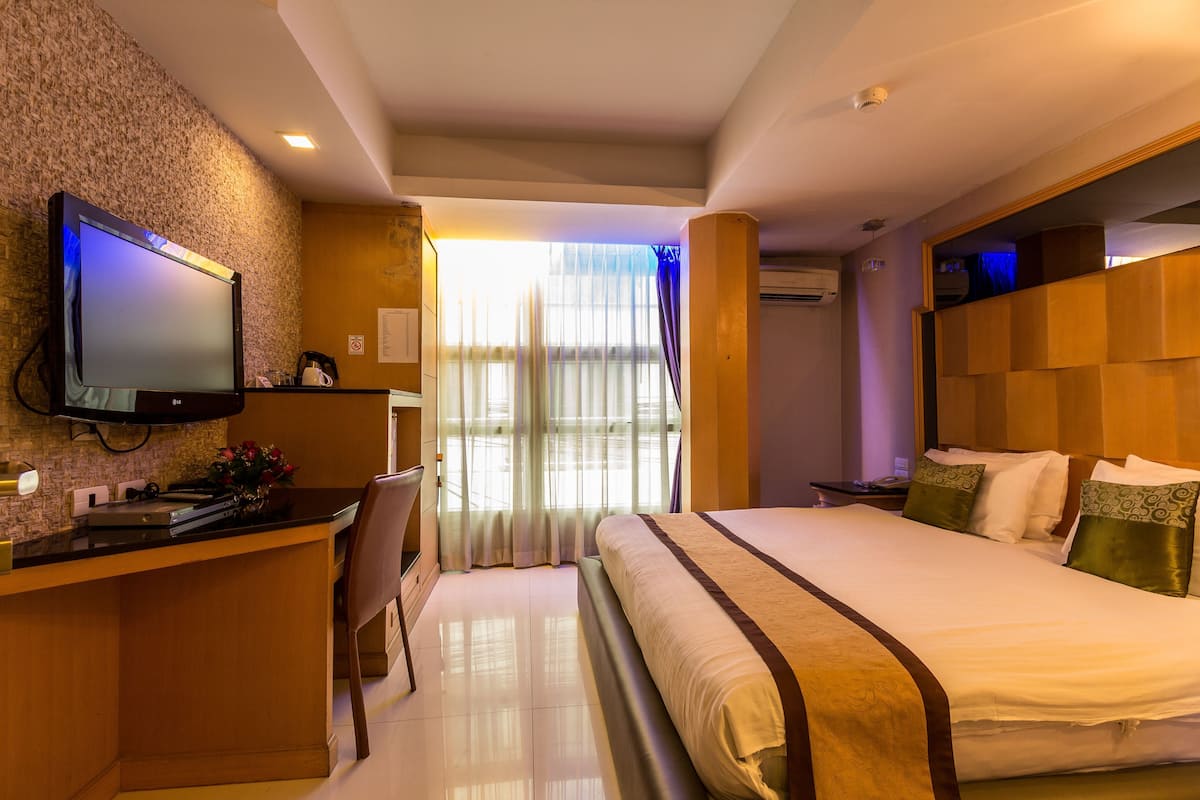 A hotel room with a bed, a desk, a television, and a window with curtains.
