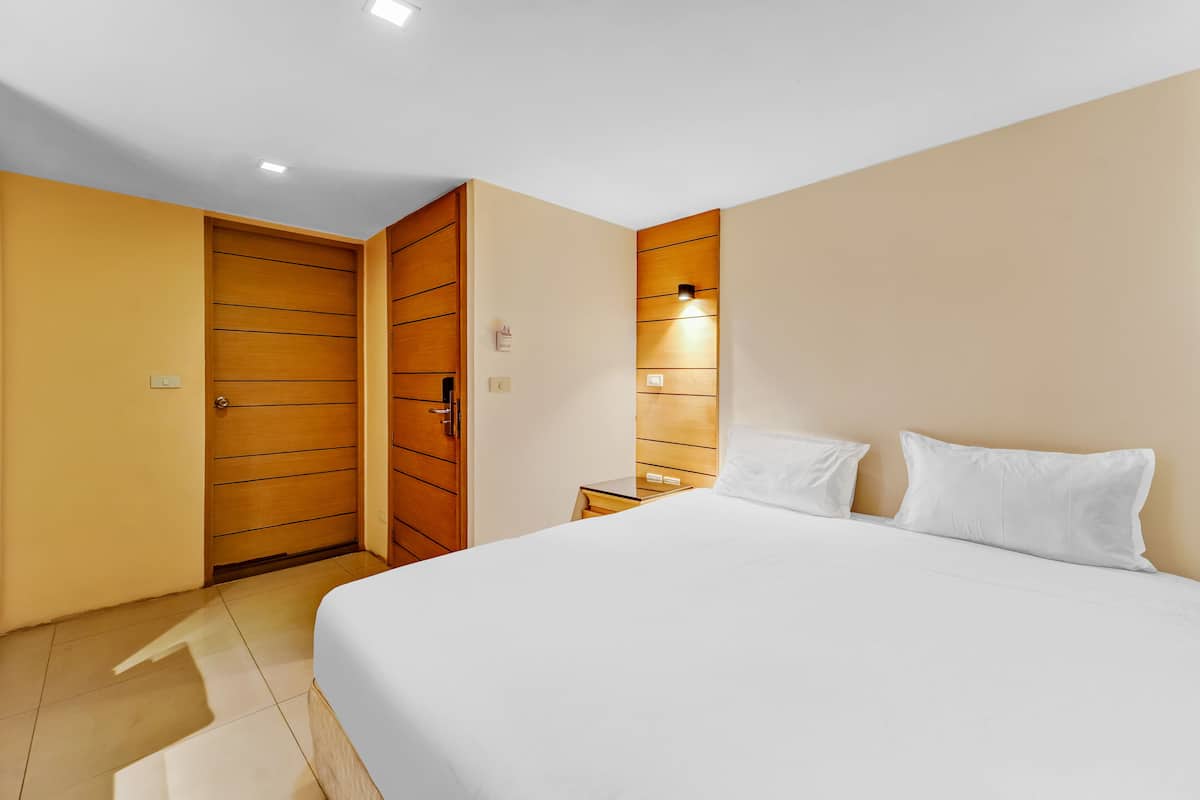 A hotel room with a large bed, wooden wardrobe, and a bedside table with a lamp.