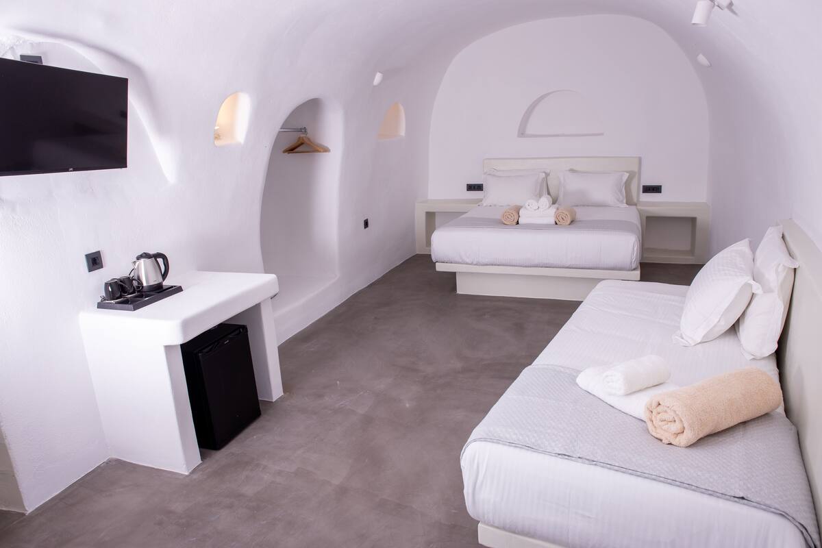A modern, minimalist hotel room with a large bed, a small desk, and a television mounted on the wall.