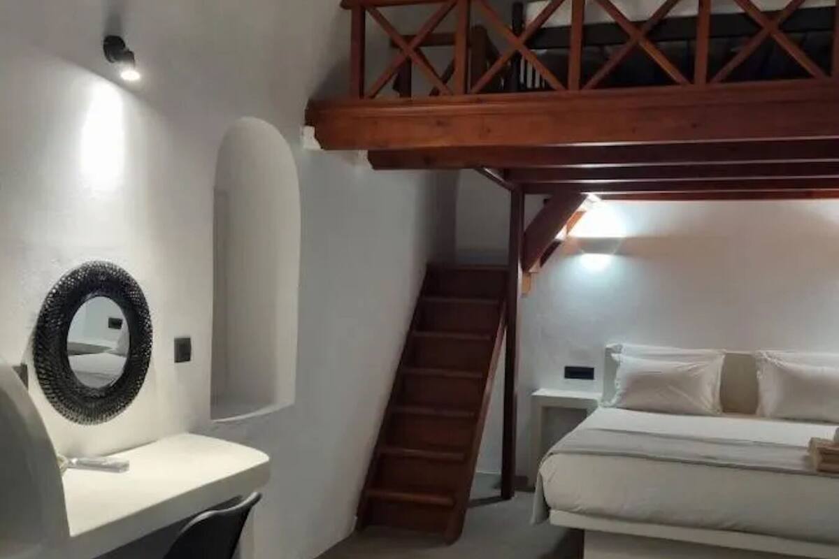 A bedroom with a bunk bed, a desk with a chair, a mirror, and a staircase leading to a loft.