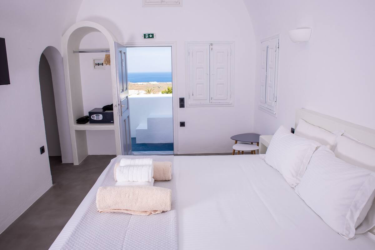 A hotel room with a bed, a desk, and a view of the sea.