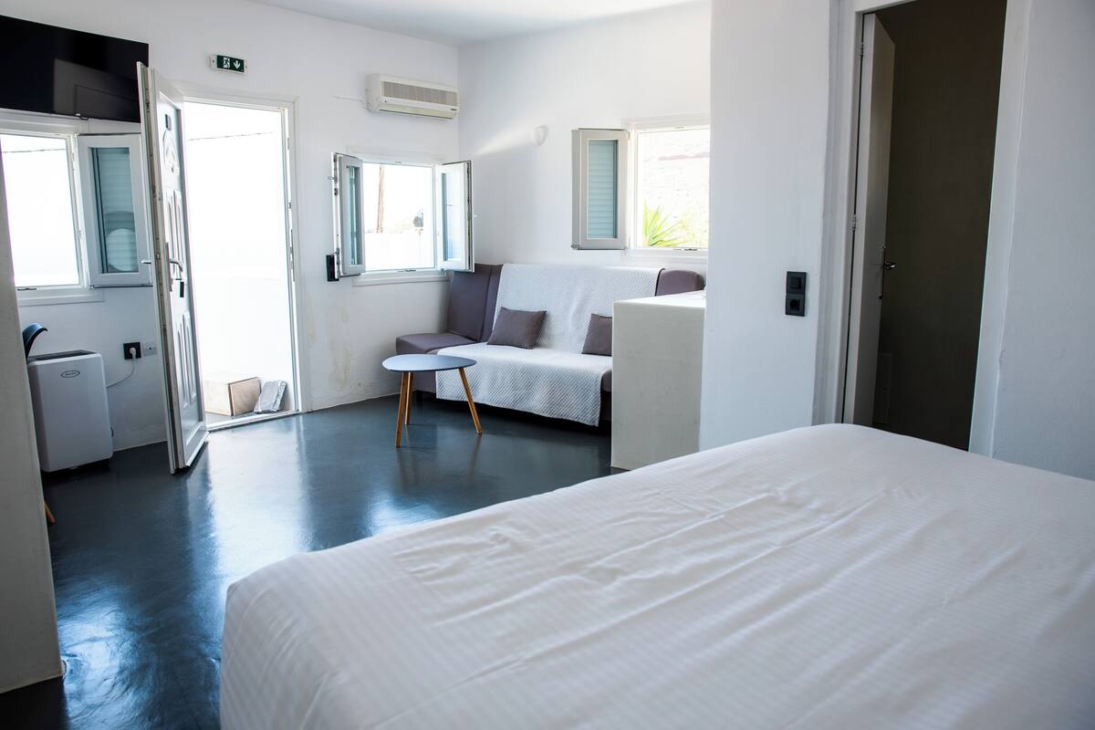 A hotel room with a bed, a sofa, a small table, and a window.