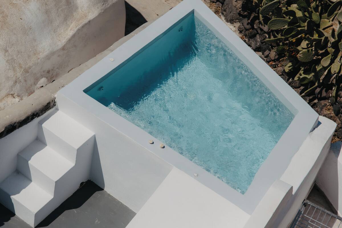 A rectangular hot tub with steps leading up to it, surrounded by a concrete wall and some vegetation.