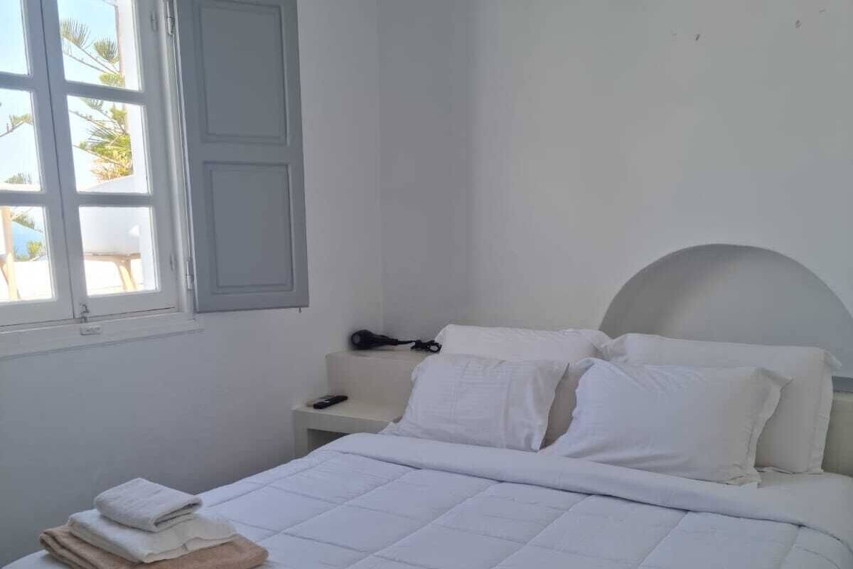 A neatly made bed with white and beige towels, a bedside table with a phone, and a window with white shutters.