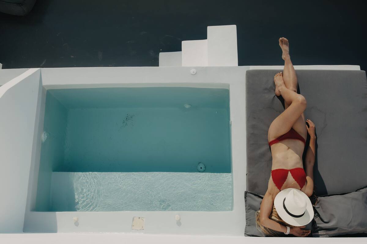 A person lying on a sun lounger next to a swimming pool.