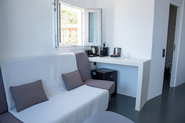 Una habitación moderna con un sofá blanco, un escritorio pequeño con una tetera y un refrigerador compacto.
