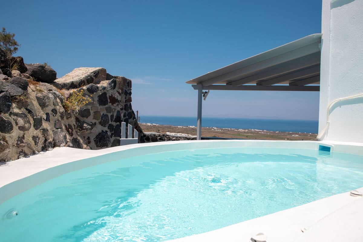 A pool with a clear view of the ocean, a stone wall, and a white building structure.