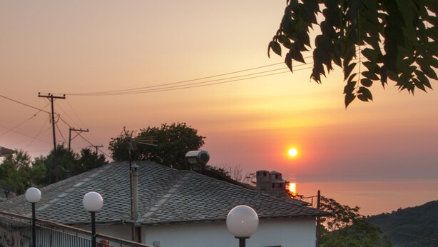 A terrace with a pool, outdoor seating, and a view of a sunset over a hill. - Astromeria Hotel (Zagora-Mouresi)