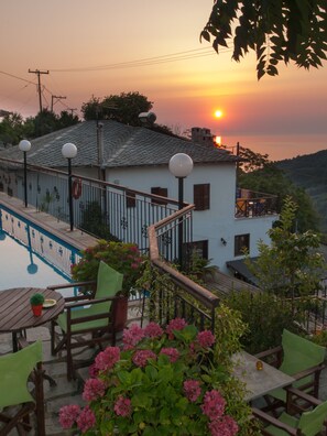 Una terraza con piscina, mobiliario exterior y vistas a un atardecer sobre una colina.