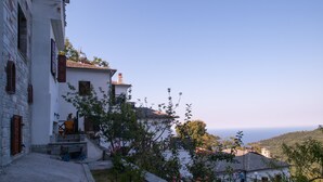 A traditional white building with a stone staircase leading to a door, surrounded by greenery and overlooking a hilly landscape. - Astromeria Hotel (Zagora-Mouresi)