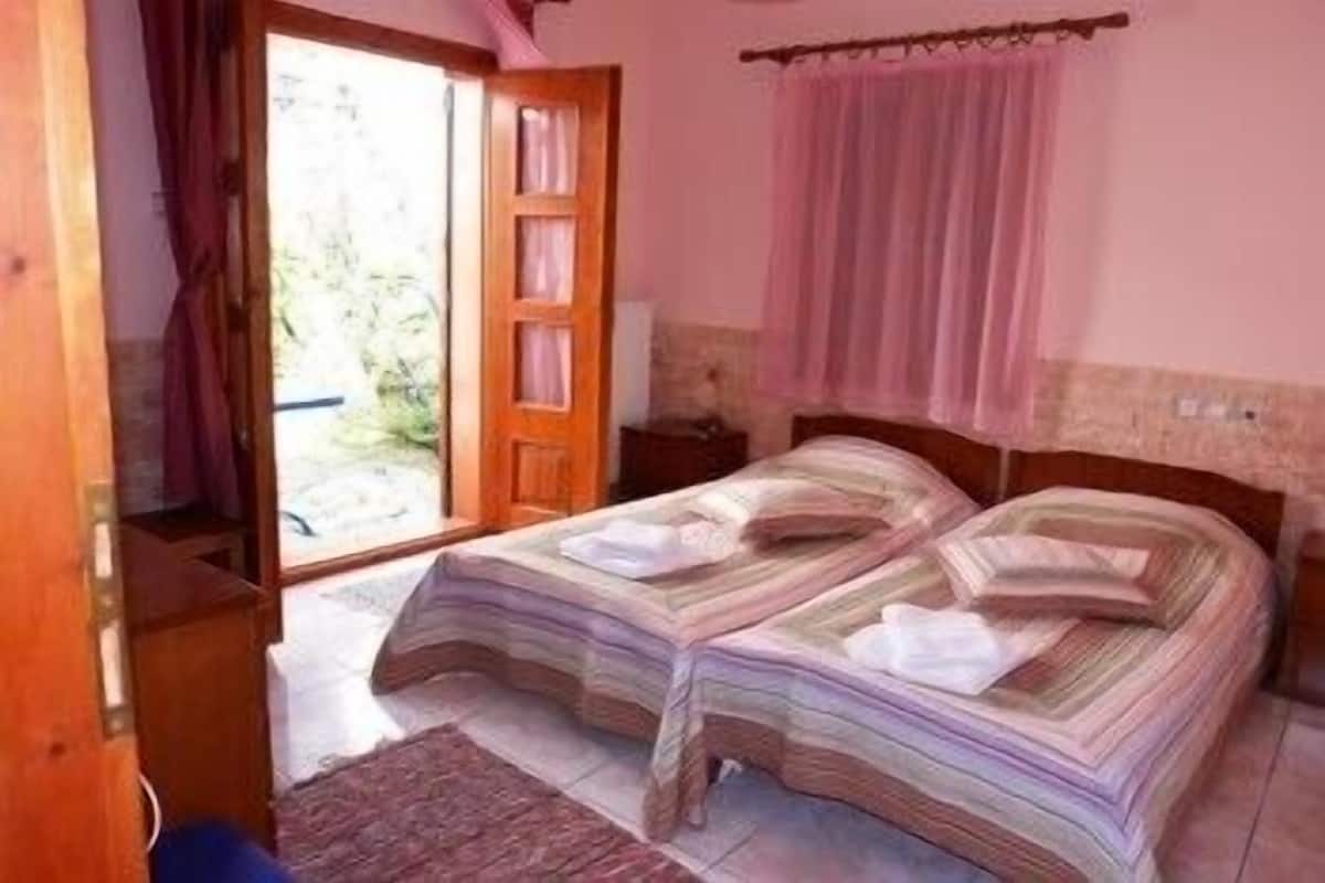 Un dormitorio con dos camas, una puerta de madera y vistas al verdor exterior.