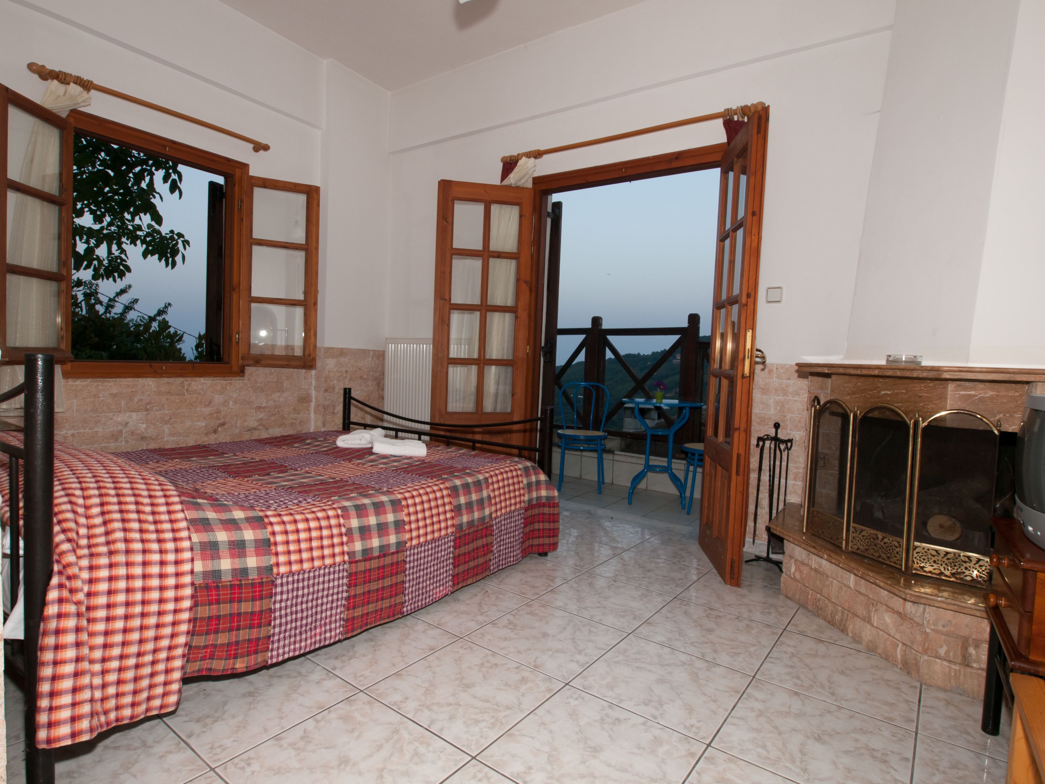 A bedroom with a bed, a fireplace, and a balcony with chairs.