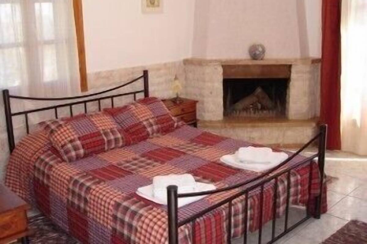 Un dormitorio con estructura de cama metálica, colcha a cuadros, mesita de noche y chimenea.