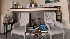 A living room with two upholstered chairs, a round coffee table, a bookshelf, and a painting on the wall. - Astromeria Hotel (Zagora-Mouresi)