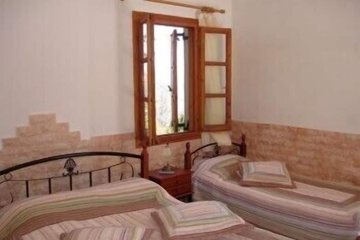 Una habitación con dos camas individuales, un cabecero de madera, una ventana con marco de madera y una pared de piedra.