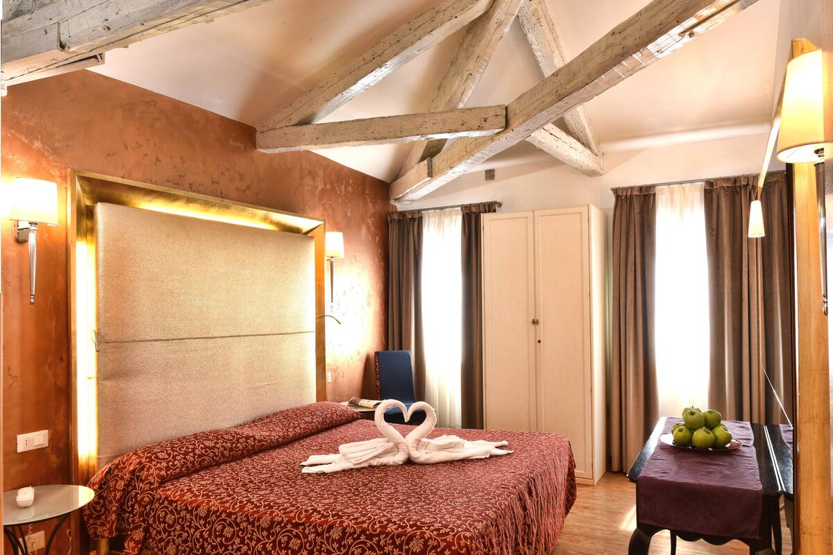 Une chambre d’hôtel avec un plafond en bois, un lit recouvert d’une courtepointe à motifs rouges, une table avec un panier de fruits et une chaise.
