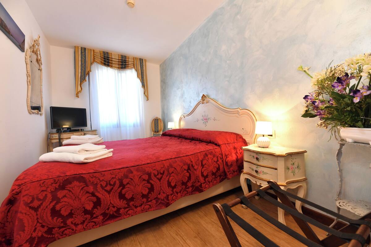 Une chambre d’hôtel avec un lit, une télévision, une table de chevet avec une lampe et un arrangement floral.