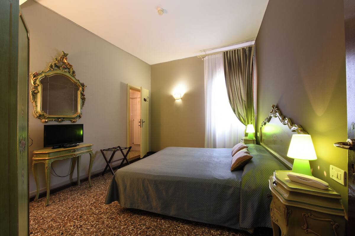 Une chambre d’hôtel avec un lit, une télévision, un miroir, une lampe et une porte.