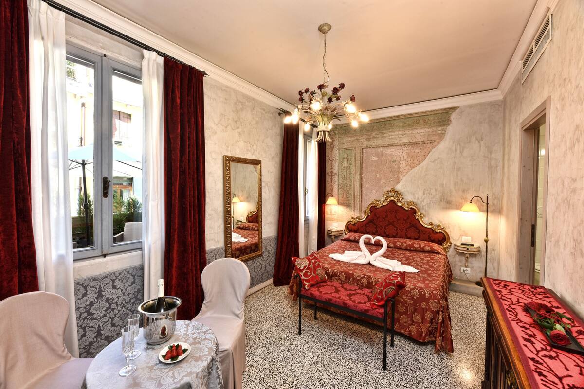 Une chambre d’hôtel avec un lit, une table sur laquelle se trouvent une bouteille et des verres, une chaise et une vue sur l’extérieur.