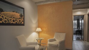 A room with two white armchairs, a small table with a lamp, and a painting of a field on the wall. - Casa Martini (Venice)