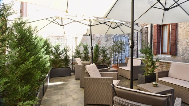 An outdoor patio area with wicker furniture, potted plants, and a brick wall. - Casa Martini (Venice)