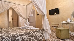 A bedroom with a four-poster bed, a television, a vanity with a mirror, and a small table with a vase and book. - Casa Martini (Venice)