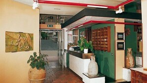 A reception area with a counter, potted plants, a large vase, and a wall-mounted clock. - Tarconte (Tarquinia)