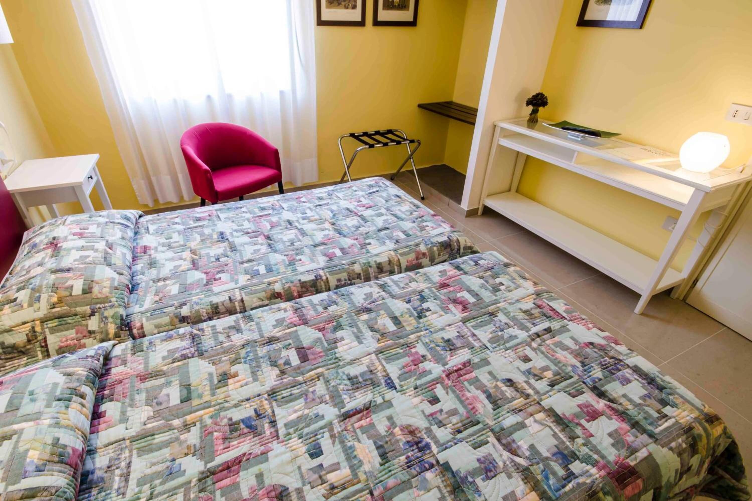 Una habitación con dos camas, un escritorio, una silla y una mesita con lámpara.