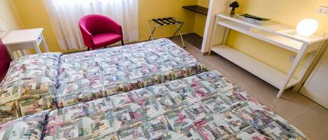 Una habitación con dos camas, un escritorio, una silla y una mesita con lámpara.