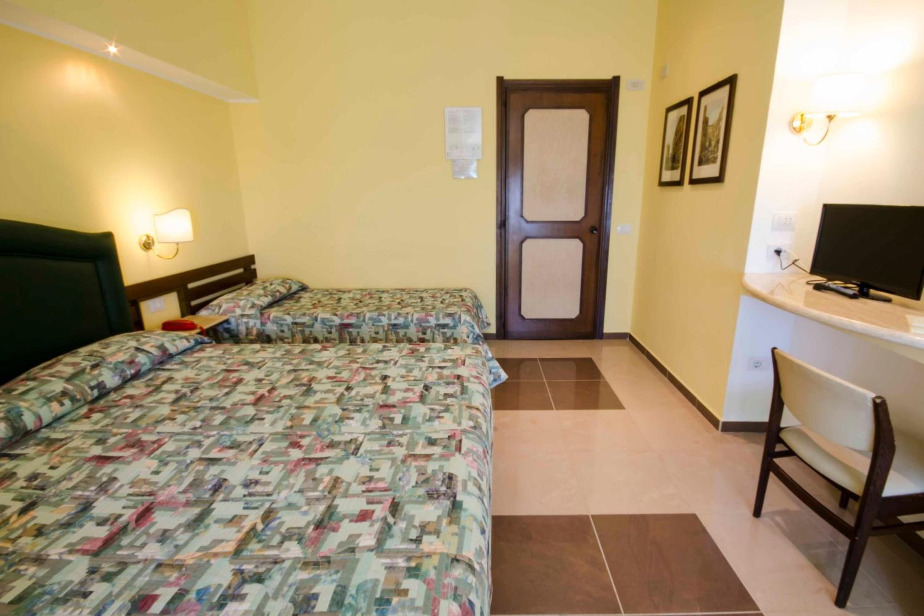 Una habitación de hotel con dos camas, un escritorio, una silla y una puerta.