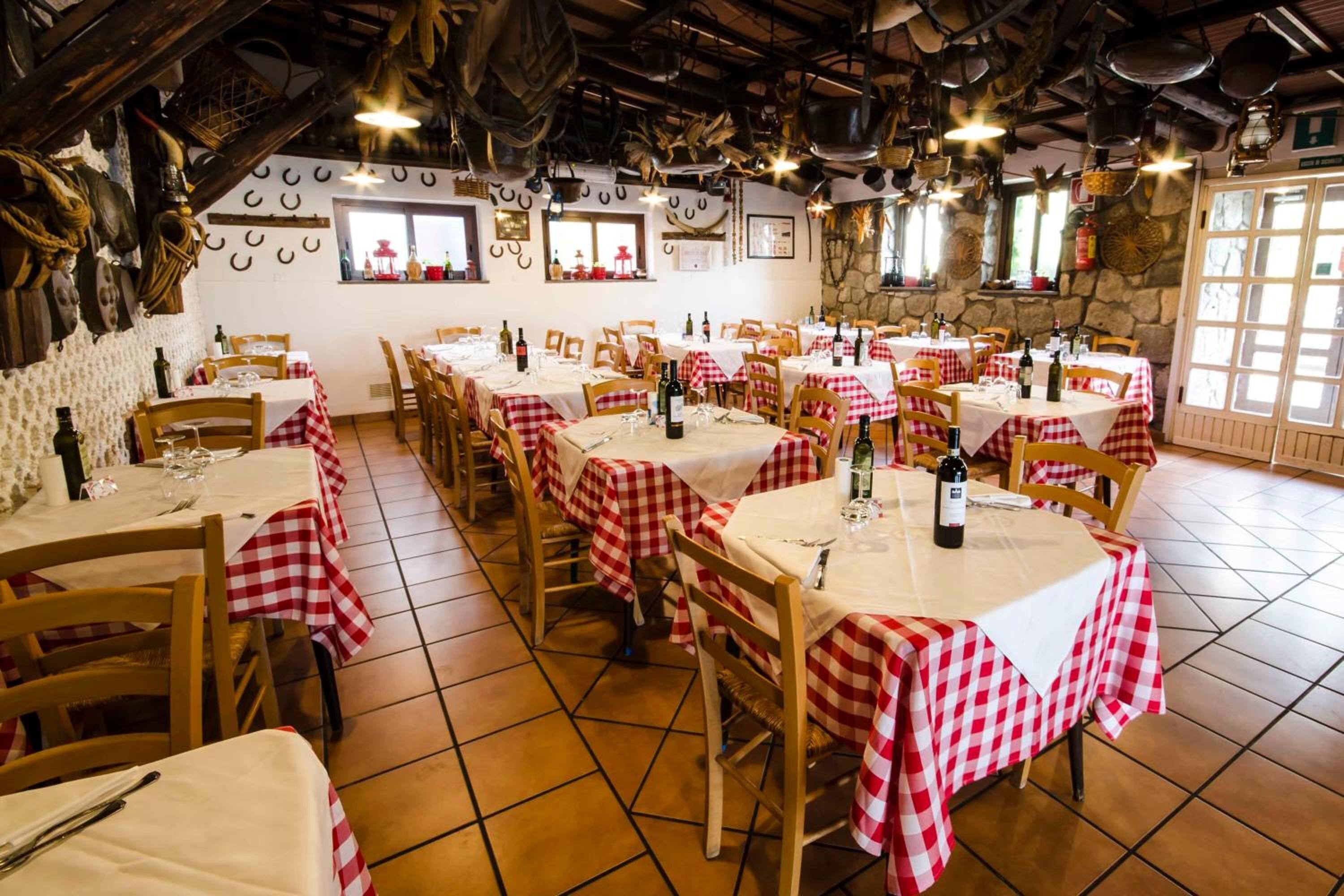 Un restaurant avec de nombreuses tables recouvertes de nappes à carreaux rouges et blancs, des chaises en bois et une bouteille de vin sur chaque table.