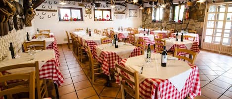 Un restaurant avec de nombreuses tables recouvertes de nappes à carreaux rouges et blancs, des chaises en bois et une bouteille de vin sur chaque table.