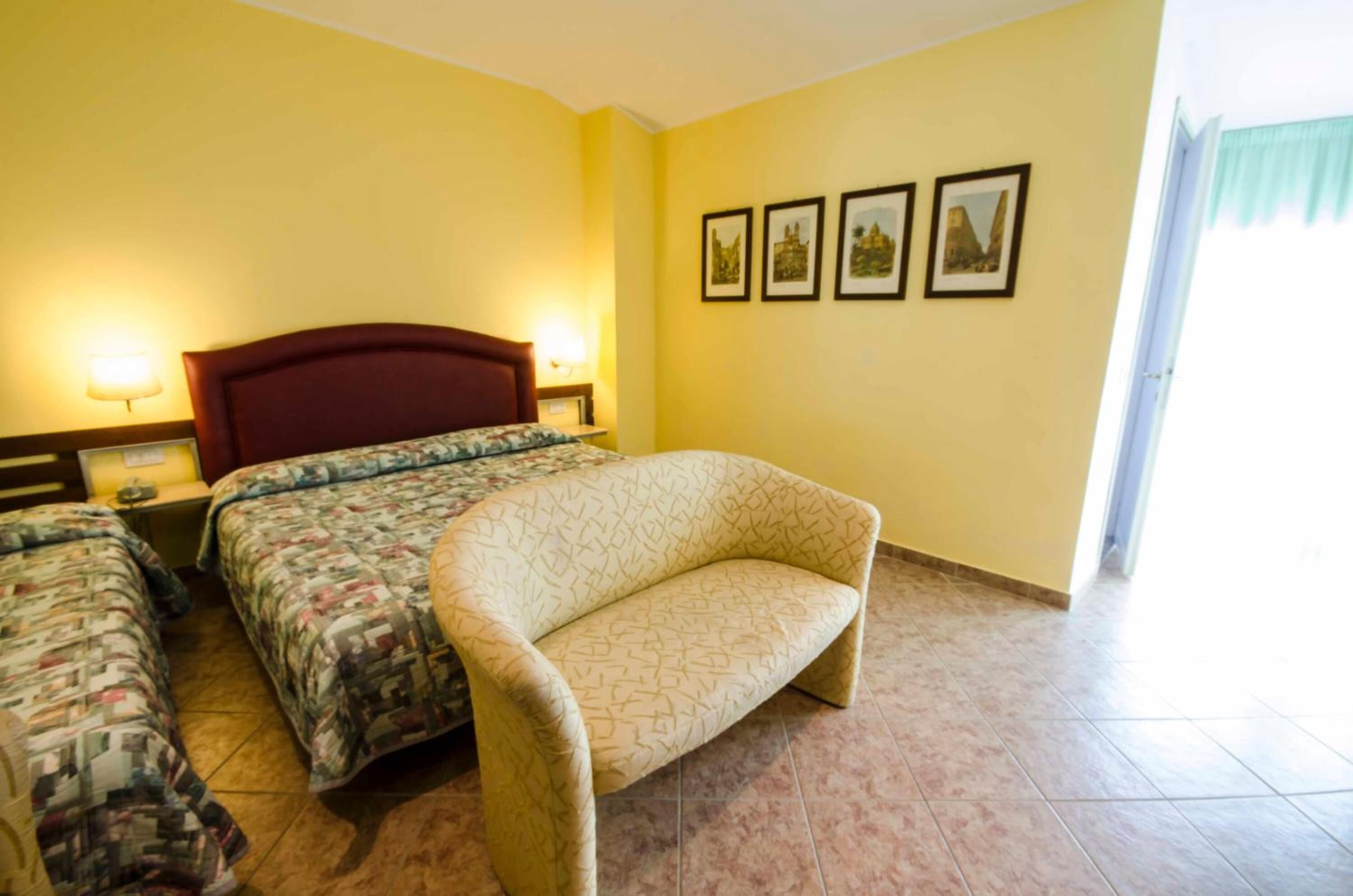 Une chambre d’hôtel comprenant un lit, deux tables de chevet, un canapé et un mur orné de quatre tableaux encadrés.