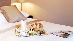 A neatly made bed with a pillow, a tray with breakfast items including bread, a cup, and a plate with fruits and a small bowl, and a magazine on the bed. - Tarconte (Tarquinia)