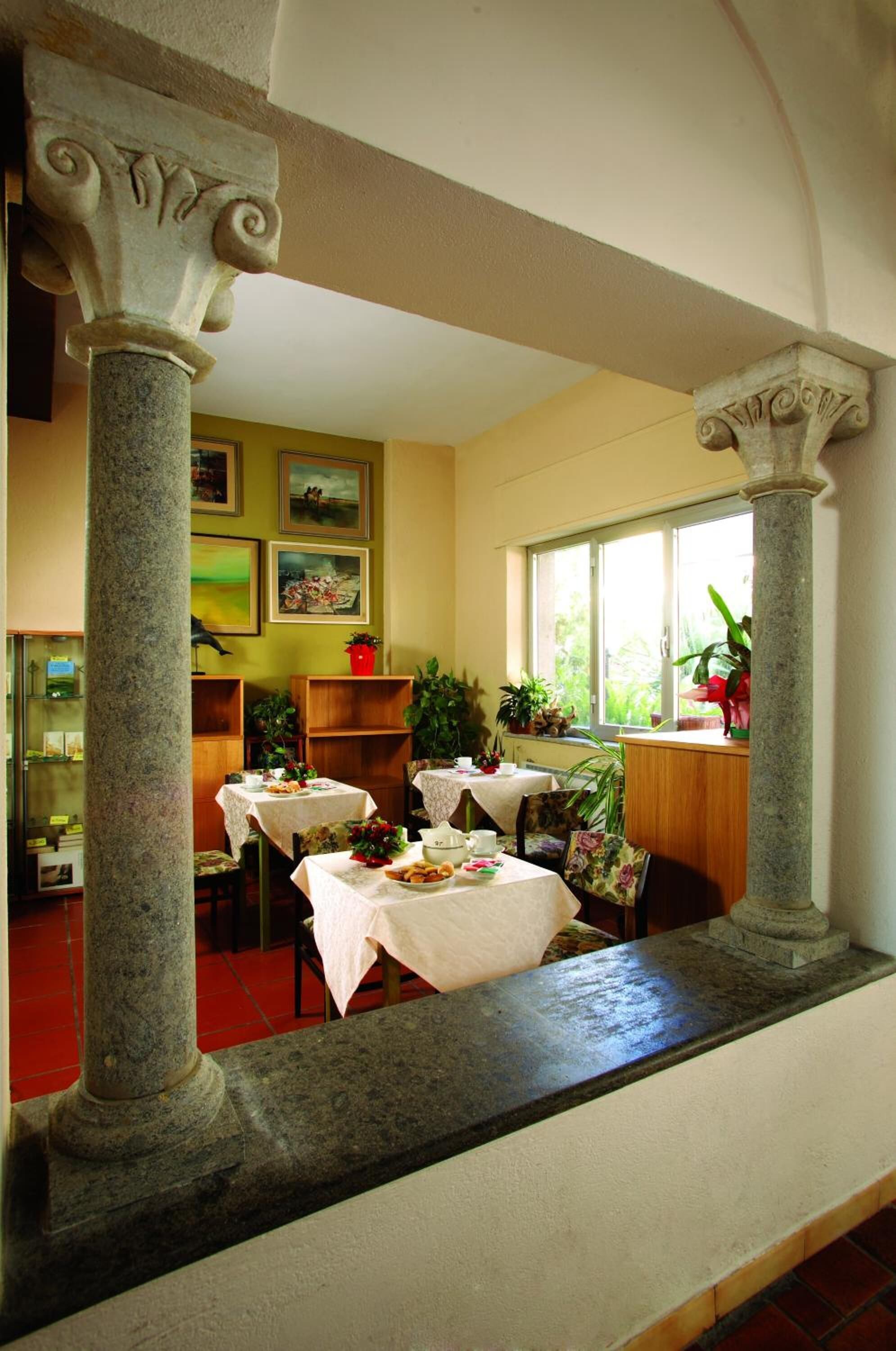 A dining area with stone columns, tables set with white tablecloths, and potted plants.
