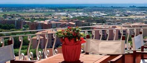 Un balcón con mesa y sillas, una planta en maceta y vistas a la ciudad.